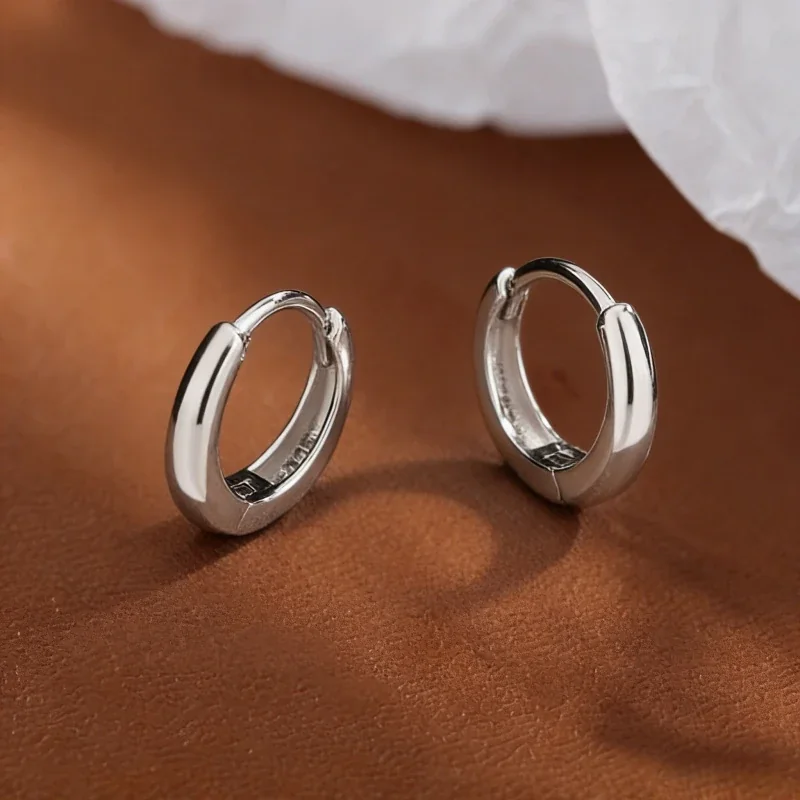 A pair of polished dome 925 sterling silver hinged hoop earrings, photographed on a white background